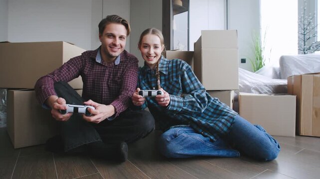 Couple plays video games together while surrounded by cardboard boxes after moving into their new home