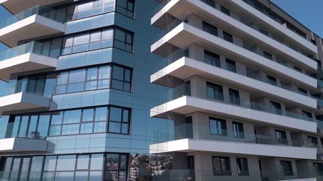 Modern apartment building facade with glass reflections and white balconies