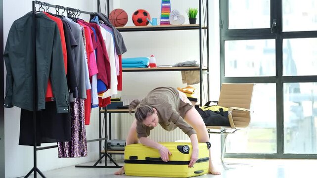 Woman traveler in comfortable home clothes struggles to close sturdy zipper of suitcase. Spacious luggage packed tightly with holiday essentials