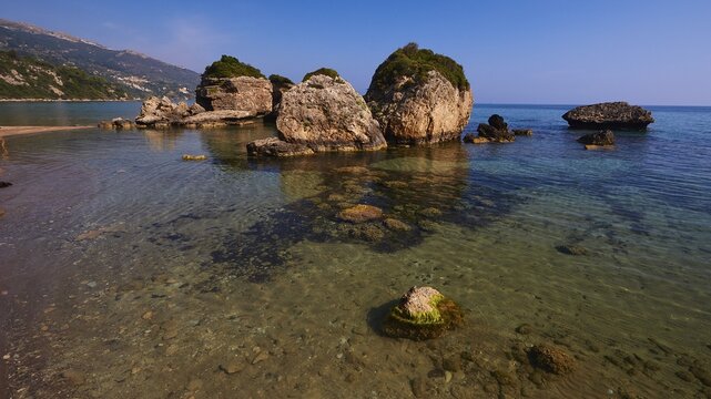 Banana Beach, offshore small rocks in the sea, green vegetation, sea green and crystal clear, small rocks visible under water, cloudless blue sky, Zakynthos Island, Ionian Islands, Greece