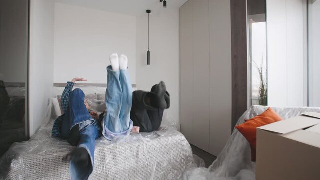 A couple and their son are falling on a bed in their new home. They are moving in with cardboard boxes around them.