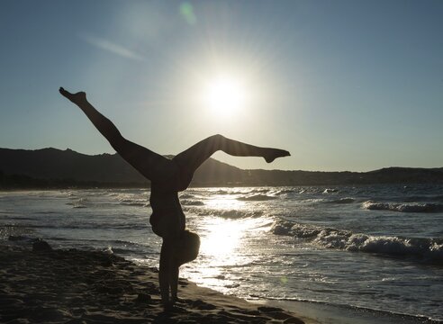 Young woman doing gymnastics on the beach, backlight, Corsica, France