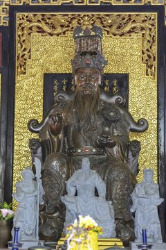 A deity seated majestically on a throne, Shou Xing (also known as Shou Lao or Nanji Xianweng), the god of longevity, carved from dark wood with gold inlays, surrounded by dragon motifs and cloud patterns, symbolises wisdom and long life in Chinese-Daoist culture, Chee Chin Khor Temple, Bangkok, Thailand