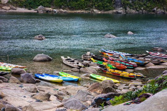 Meghalaya, India - 31 March 2023: View of colorful wooden boats moored on the rocky banks of the Dawki River with clear water and surrounding hills.