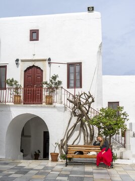 Young woman with red skirt sitting on a bench with sleeping cats, Cycladic white houses, Panagia Tourliani Monastery, Ano Mera, Mykonos, Cyclades, Greece