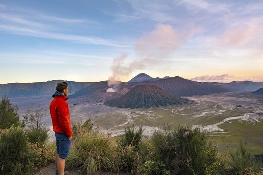 Young man in front of volcanic landscape at sunset, view in Tengger Caldera, smoking volcano Gunung Bromo, in front Mt. Batok, in the back Mt. Kursi, Mt. Gunung Semeru, National Park Bromo-Tengger-Semeru, Java, Indonesia