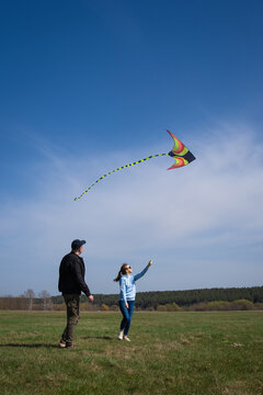 Young couple embracing freedom and recreation together, flying a vibrant kite high in the clear blue sky over an expansive green meadow in the countryside. Vertical photo