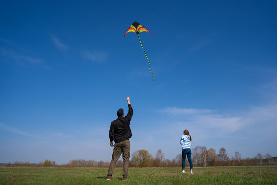 Couple flying a colorful kite over a wide green field under a clear blue sky, enjoying a sunny, carefree day outdoors - fun, peaceful, and full of joyful togetherness