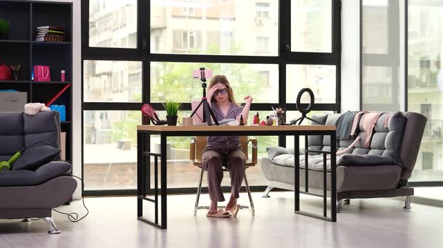 Confident young girl sits at table and creates beauty vlog. Child surrounded by charming beauty accessories and neatly arranged cosmetic items