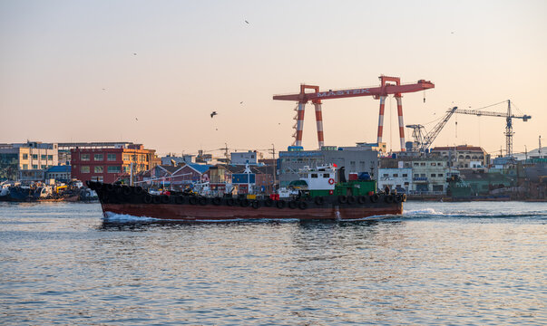 Busan, Busan, South Korea - 21 February 2026: View of a cargo ship navigating the harbor with industrial cranes and buildings in the background.