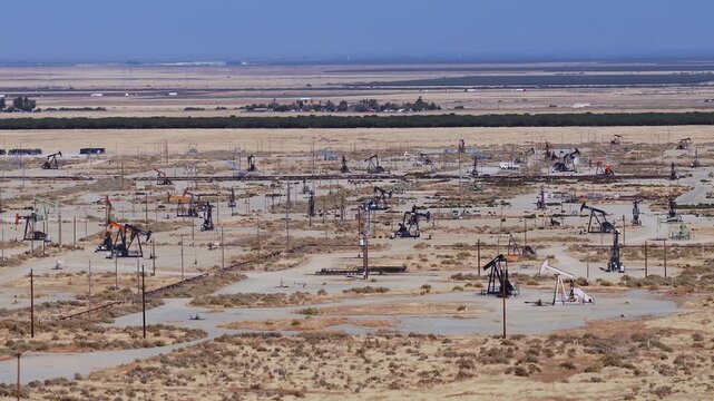 Aerial view shows numerous pump jacks extracting crude oil across an arid Californian oil field, illustrating industrial energy production and resource management in the Central Valley.