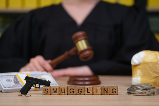 In a courtroom setting, a judge prepares to deliberate on a smuggling case. A gavel sits poised, alongside cash, a firearm, and handcuffs, representing the gravity of the situation.