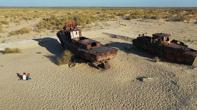 Aerial view of an artist painting abandoned stranded shipwrecks in the Aral Sea desert.