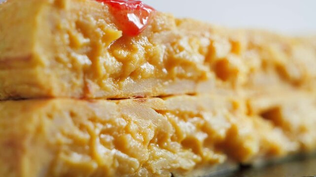 Close up of Spanish potato omelette Tortilla de patatas slices topped with grated tomato, a traditional Spanish dish. 