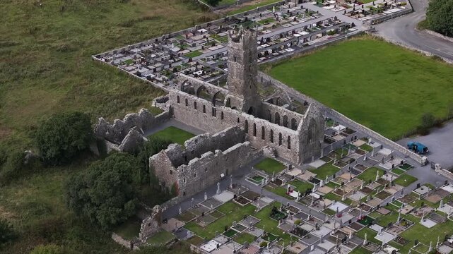 High angle aerial shot of the 13th century Claregalway Abbey ruins and surrounding graveyard in County Galway, Ireland. Perfect for travel documentaries and historical heritage content.