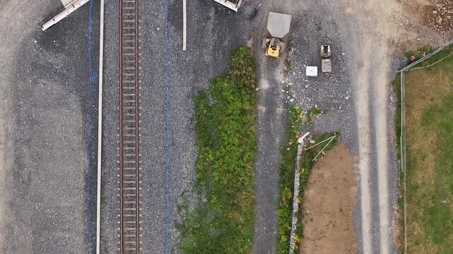 A topdown drone shot following existing train tracks to reveal an active construction site where workers are adding a second route, highlighting infrastructure growth and ecofriendly transport.