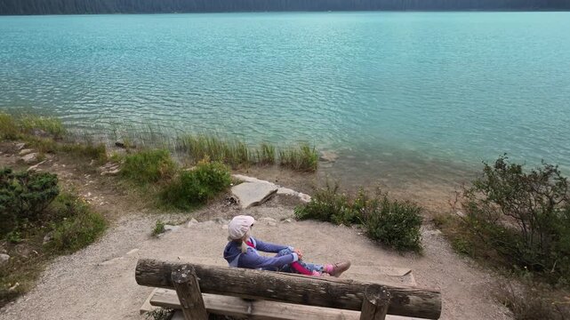 top view of Woman wearing sunglasses relaxing on a wooden bench overlooking the stunning turquoise waters of Emerald Lake with surrounding mountains in Yoho National Park, British Columbia, Canada