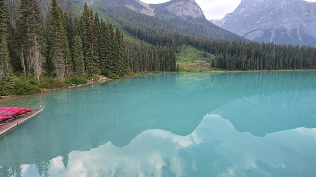 Red canoes on turquoise water of Emerald Lake, surrounded by dense forest of evergreen trees and mountains reflecting in the calm surface during summer in Yoho National Park, British Columbia, Canada