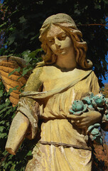 Obraz premium Weathered stone angel statue holding flowers, symbolic memorial sculpture representing remembrance, grief, eternal love, hope and peace.