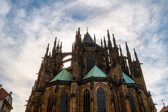 Prague, Czechia - 08 May 2023: View of St. Vitus Cathedral featuring intricate Gothic architecture, pointed spires, and green copper roofs set against a cloudy sky.