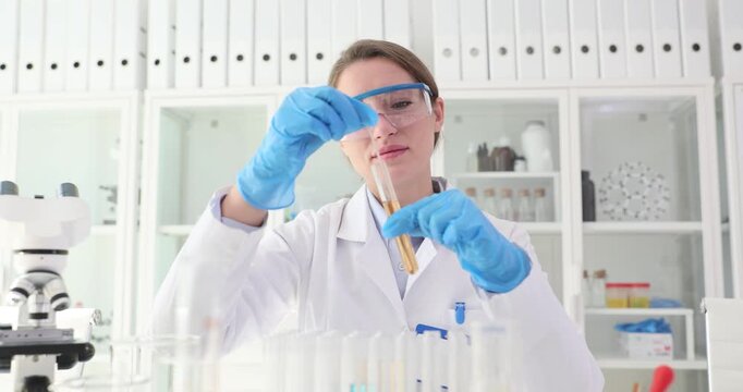 Female assistant in gloves stirs liquid in test tube with long stick in lab slow motion. Skilled chemist researches color fluid with modern techniques