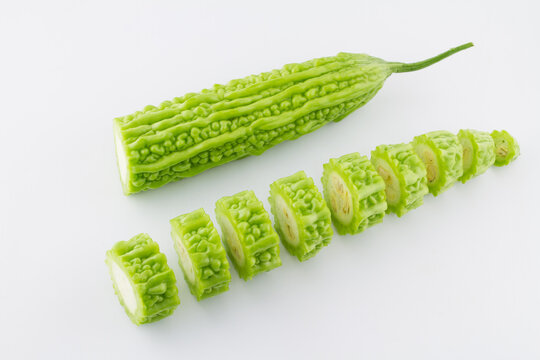 Whole fresh bitter melon and sliced pieces arranged on a plain white surface, showing its bumpy texture and cross-seeds.