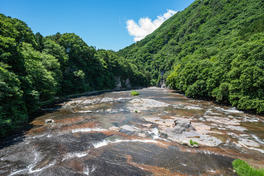 青空の下、豊かな緑の渓谷を流れる清らかな川と岩肌の美しい風景