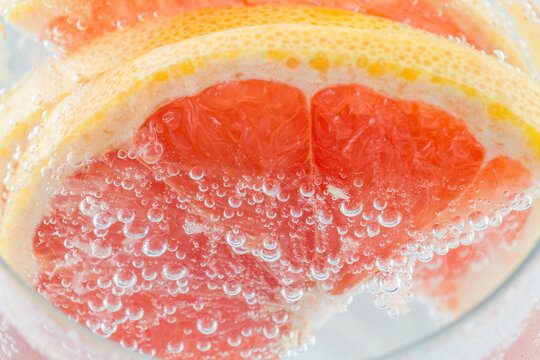 Close-up of fresh pink grapefruit slices submerged in bubbly clear sparkling liquid, showing juicy pulp and yellow peel.