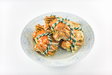 Three cooked crabs tied with rope, served on a light blue patterned plate against a plain white background. © tai