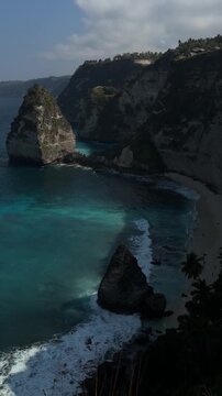 A scenic coastal view featuring a rocky cliff, turquoise waters, and a distant island. The sky is partly cloudy, creating a serene atmosphere.