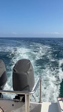 A boat's motor with a view of the ocean waves and clear blue sky. The scene captures the essence of boating and water activities.