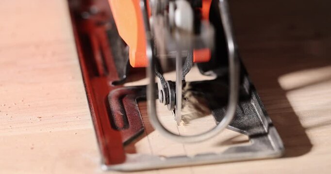 Electric jigsaw blade cuts through wooden board in detailed view. Rapid metal blade slices material leaving narrow path across timber surface