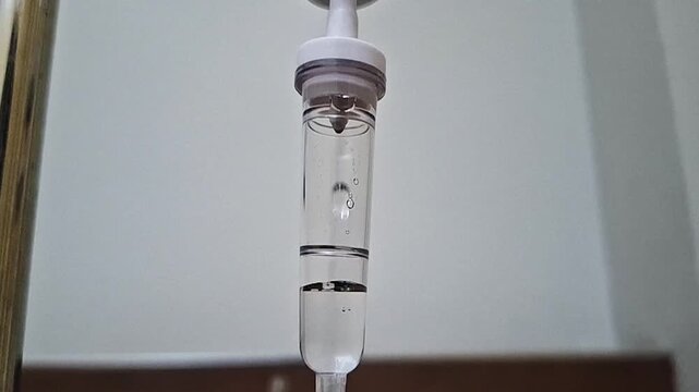 Close-up shot of liquid dripping slowly inside a medical IV drip chamber in a clinic or hospital setting