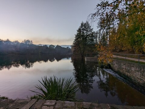 Calm autumn pond reflecting trees beside a small weir