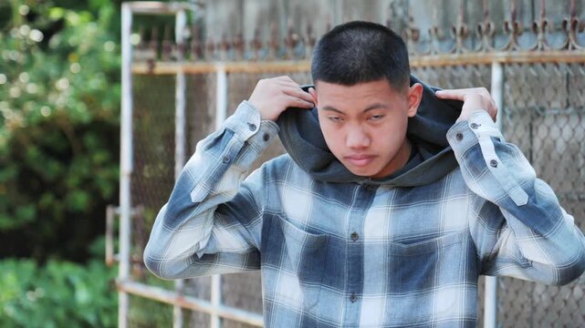 young Asian teenage boy with a buzz cut hairstyle and smiles gently while standing outdoors, wearing a blue plaid hoodie