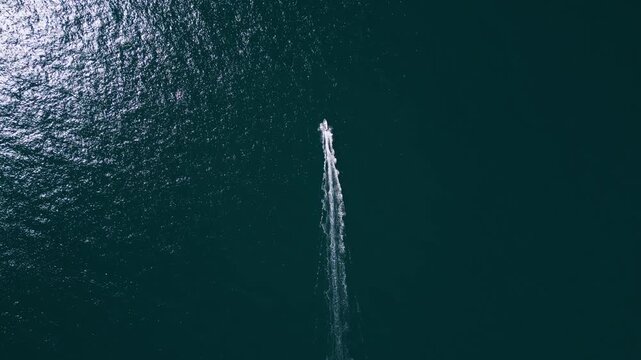 Aerial top down view of a motorboat speeding across deep blue ocean water