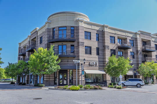 Wilmington, North Carolina, United States - 04 September 2026: View of Mayfaire Town Center featuring a brick building with balconies, retail storefronts, and trees under a clear blue sky.