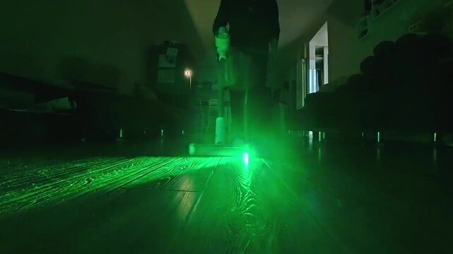 Vacuum cleaner using green light to reveal dust on dark floor.   