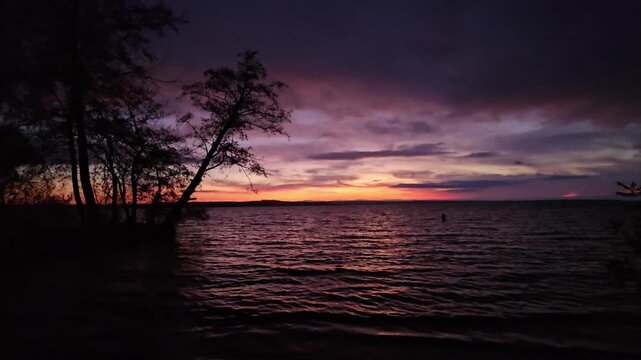 Scenic sunset over a massive reservoir lake in autumn with alder trees and colorful cloudy sky at dusk