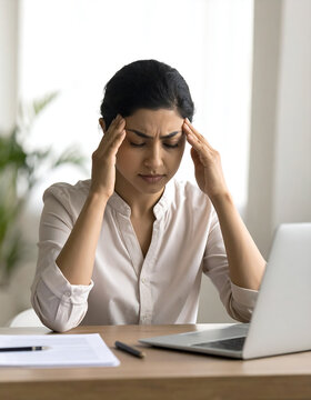 Stressed young woman suffering from a headache while working at her desk with a laptop computer