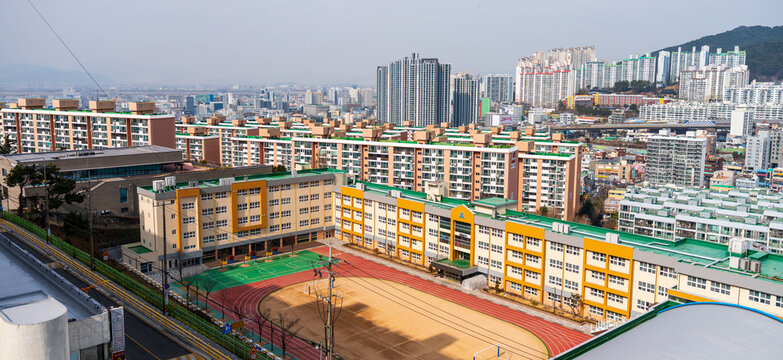 Busan, South Korea - 07 February 2026: View of a school building with a running track and playground surrounded by dense residential apartment blocks in the city.