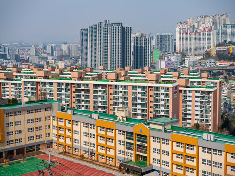 Busan, South Korea - 07 February 2026: View of a modern school building with a yellow and orange facade and a green roof, set against a dense residential area with high-rise apartments.