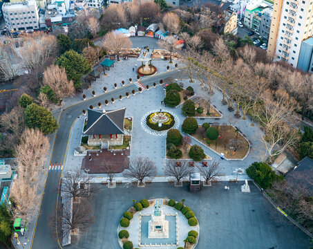 Busan, South Korea - 07 February 2026: View of the Yongdusan Park plaza featuring a central statue, traditional pavilion, paved walkways, and bare trees during winter.