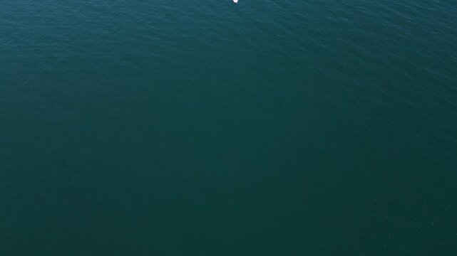 Aerial top down view of a motorboat speeding across deep blue ocean water