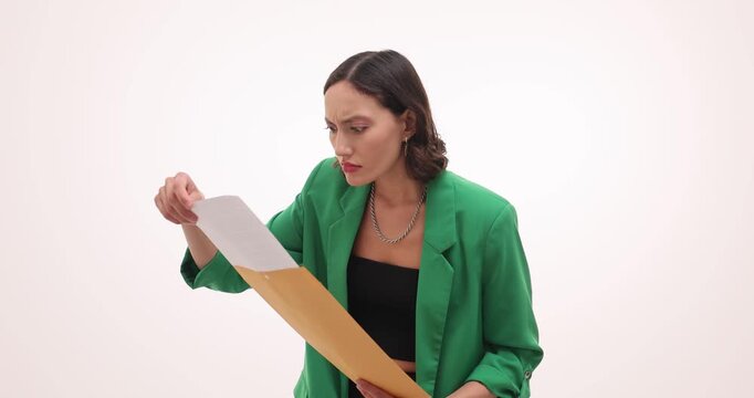 Shocked woman in green blazer holds letter against white background. Surprised reader covers mouth with hand reacting strongly to written message
