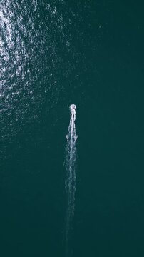 Aerial top down view of a motorboat speeding across deep blue ocean water