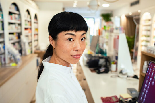 Pharmacist looking at camera behind counter in pharmacy