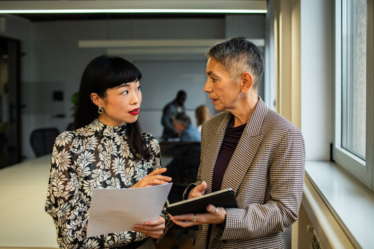 Two coworkers discussing paperwork by an office window