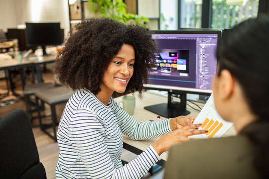 Designer discussing bar chart with colleague at computer