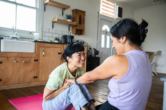 Two women doing partner stretch on yoga mat at home